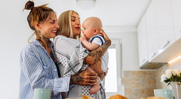 A female couple hugging their foster baby in the kitchen