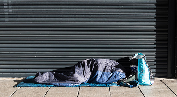 rough sleeper covered in a sleeping bag on the ground with their belongings in bags