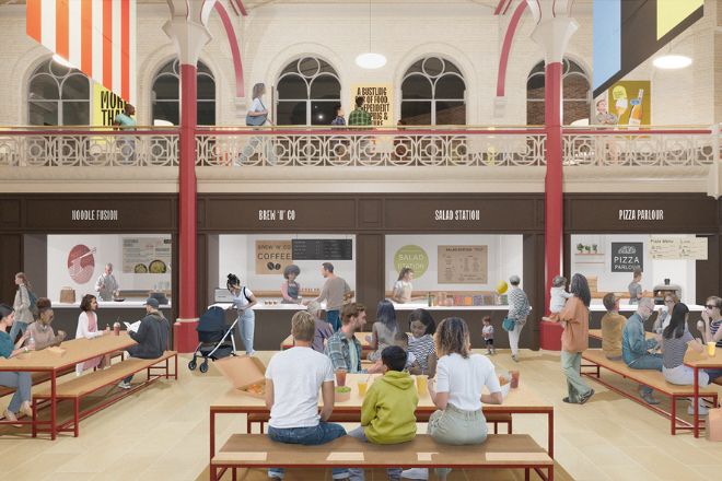 Indoor market scene with people seated at communal tables and ordering from various food stalls. Balconies, arched windows, and a high ceiling enhance the spacious atmosphere.