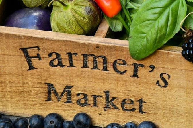 A close up of a wooden box containing fruit and vegetables, carved with the text Farmers Market