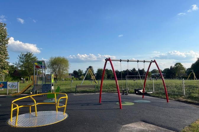 A sunny playground with new equipment including swings and a roundabout