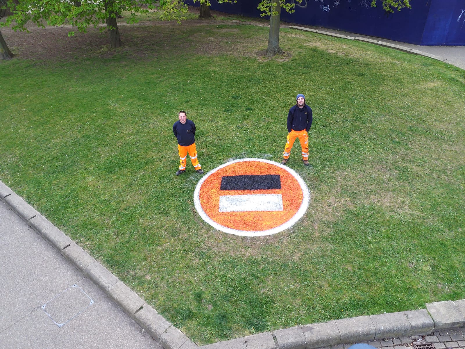 Two people standing next to the Stephen Lawrence Day Foundation logo on a green space