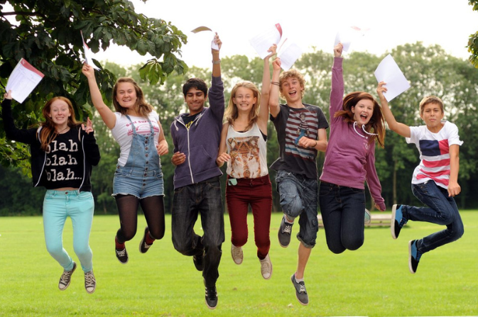 Several teenagers jump in the air with exam results