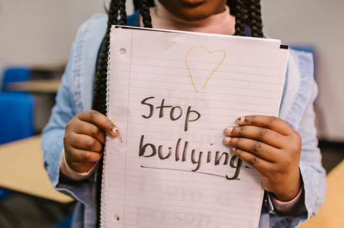 A close up of a child holding up a notebook. On the notebook is handwritten text that reads 'Stop Bullying'