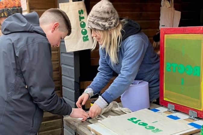 A young man is guided by a woman as he tries his hand at screen printing
