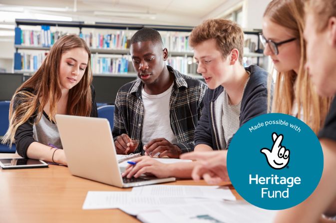 four teenagers sit in a library gathered abound a laptop discussing a project