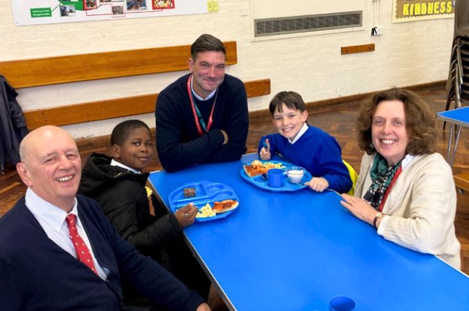 Council representatives sitting at a table with two children having a school lunch