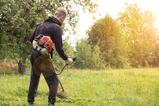 A man uses a strimmer to cut grass