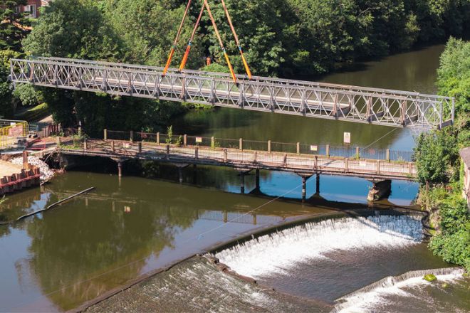 A pre-fabricated walkway being lifted above an older structure.