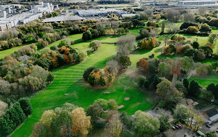 Aerial view of Sinfin Golf Course with city skyline in background.