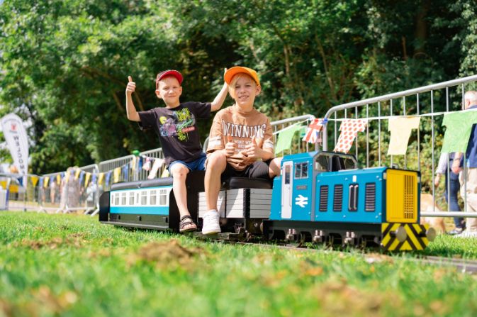Two smiling boys riding on a miniature railway