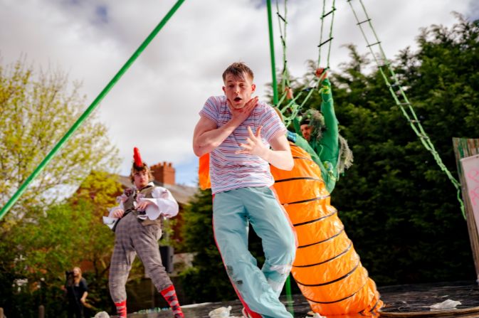 Two performers on a stage. The man in the front is holding his throat and grimacing