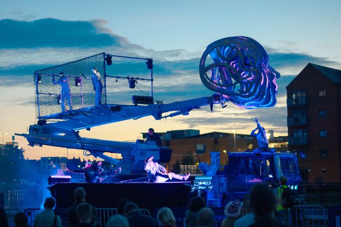 Performance artists on an aerial platform against a darkening evening sky