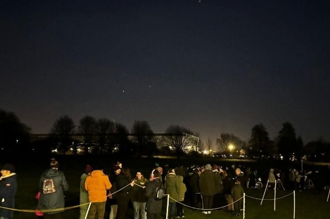 A group of people standing in a park looking up at the night sky