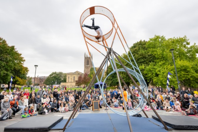 A crowd watches an outdoor show with two circus performers inside a spinning metal wheel