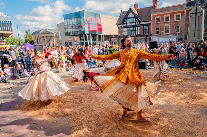 Dancers in traditional Indian costume perform in a sunny Derby Market Place, watched by a crowd