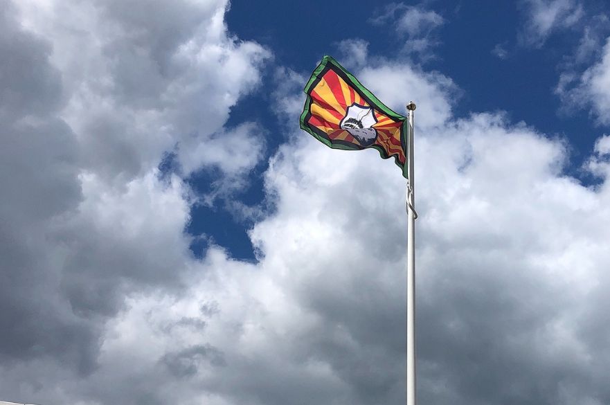Windrush flag flying from a flag pole against blue, cloudy sky.
