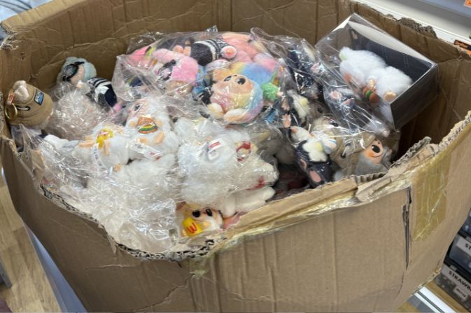 Large cardboard box filled with small soft toys in plastic wrappeing.
