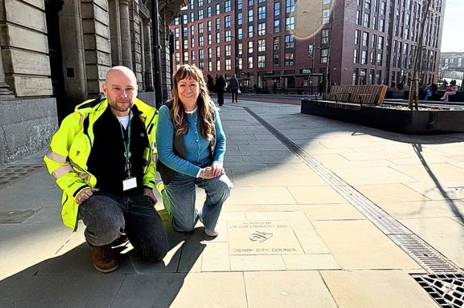 A man and woman kneeling next to an engraved slab that says funded by UK government.