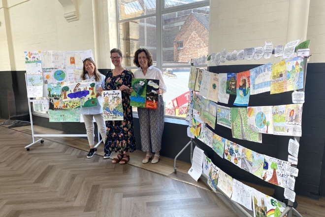 Three women stood in front of an exhibition stand displaying artwork.