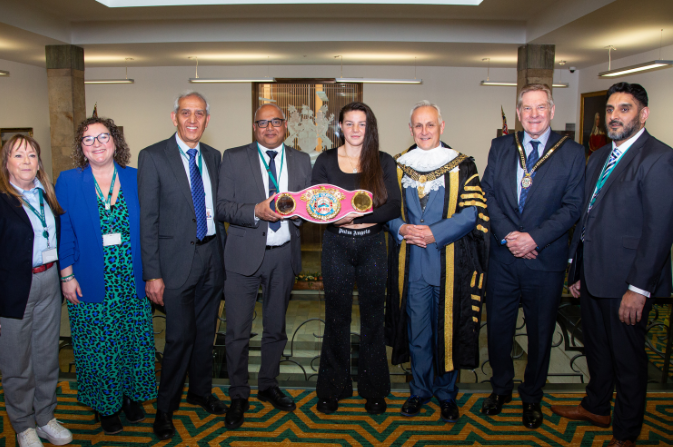 sandy ryan stands holding her championship belt surrounded by Derby City Council councillors