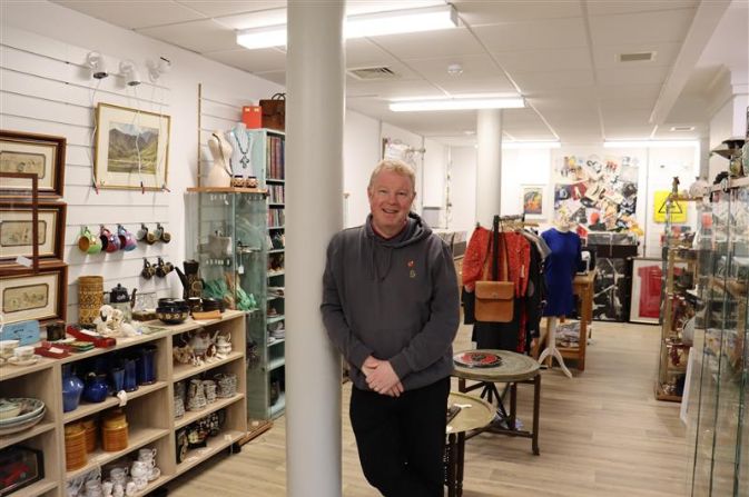 A man leaning against a post in a store filled with ornaments and decor.
